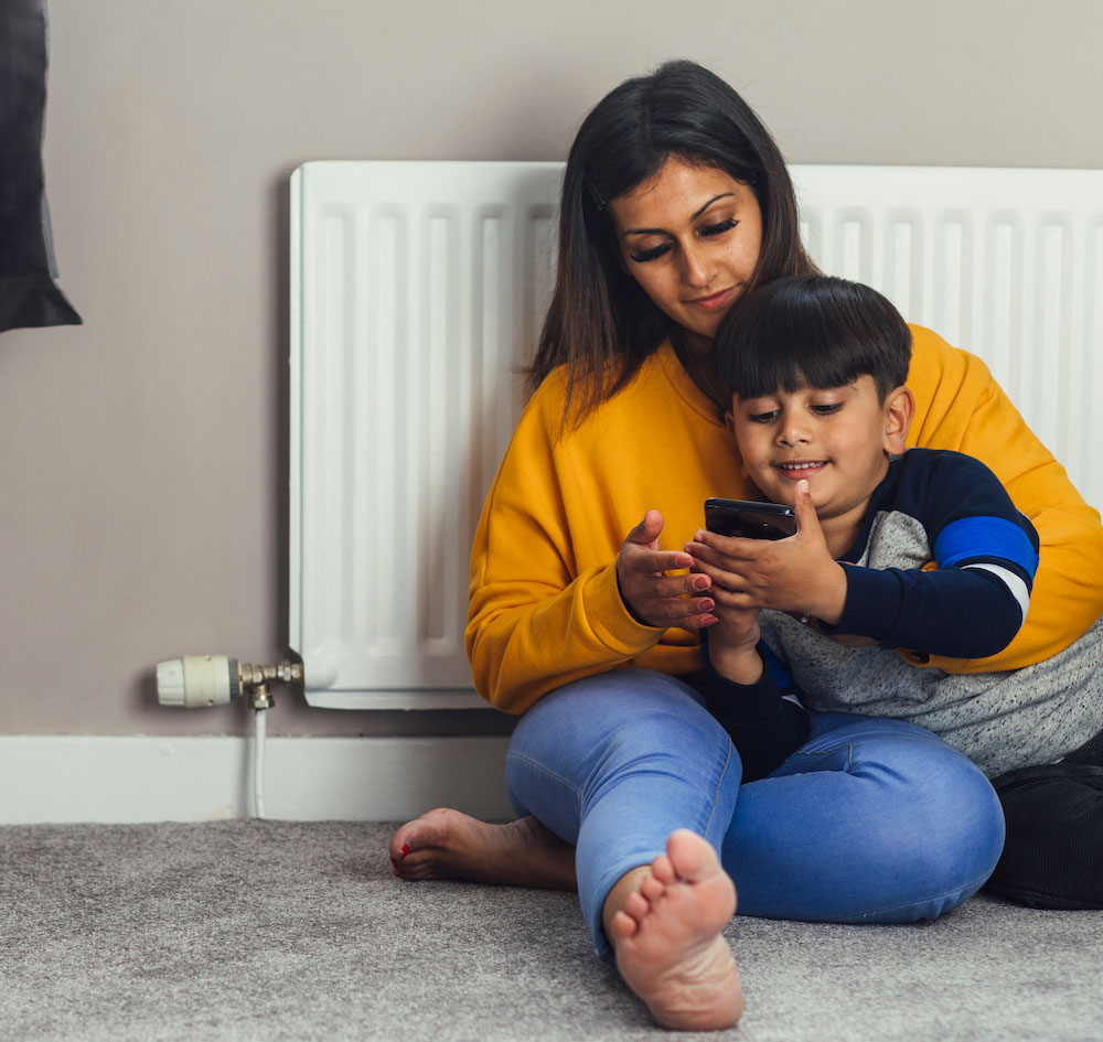 Family sitting beside a standard white convector radiator